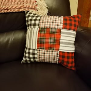 Può includere: Un cuscino patchwork con un motivo a quadri nero, bianco e rosso. Il cuscino è realizzato con tessuti diversi e ha una forma quadrata.