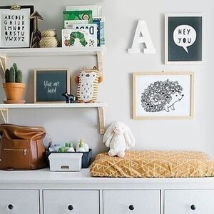 May include: A white dresser with four drawers, a changing pad with a yellow and brown geometric pattern, and a white shelf with various items, including a black and white print of a hedgehog with flowers, a black chalkboard with the text "You are loved", a brown leather diaper bag, and a white stuffed bunny.