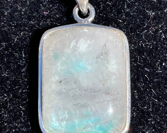May include: A silver pendant with a rectangular clear quartz stone with blue inclusions. The stone is set in a silver bezel.