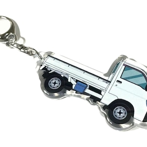 May include: White truck keychain made of clear acrylic. The truck is a small pickup truck with a white cab and a blue bed. The keychain has a silver metal ring.
