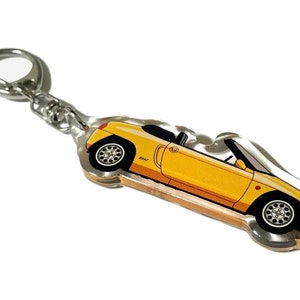 May include: A yellow convertible car keychain with a silver key ring. The car is a cartoon illustration of a sports car with a black interior and black wheels.
