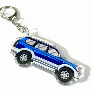 May include: Blue and silver car keychain with a silver key ring. The car is a cartoon illustration of a Toyota Land Cruiser.