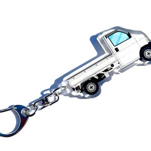 May include: A white truck keychain with a silver metal chain and a silver metal ring. The truck is a small pickup truck with a flatbed.