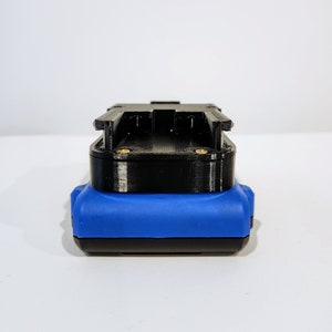 Op de afbeelding: Een zwarte en blauwe batterijpack met een plastic behuizing. De batterijpack heeft een sleuf voor een batterij en een connector aan de zijkant.