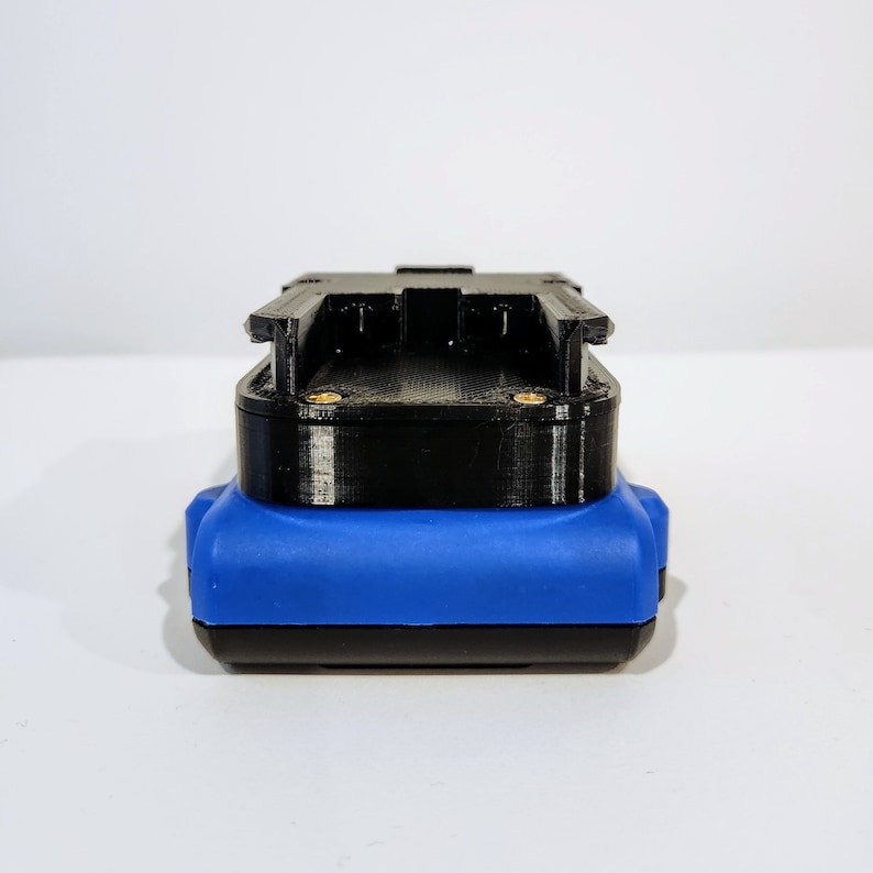 Op de afbeelding: Een zwarte en blauwe batterijpack met een plastic behuizing. De batterijpack heeft een sleuf voor een batterij en een connector aan de zijkant.