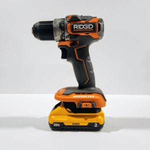 May include: A black and orange cordless drill with a black and orange battery pack. The drill is labeled "RIDGID" and "BRUSHLESS". The battery pack is labeled "20V" and "DEWALT".