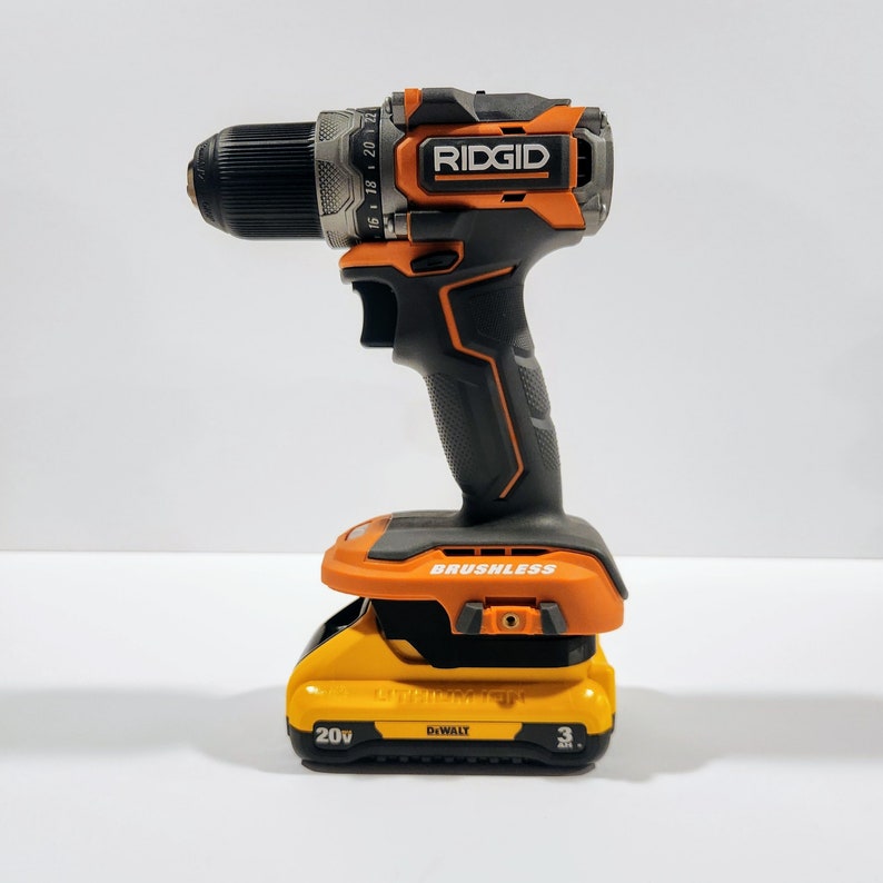 May include: A black and orange cordless drill with a black and orange battery pack. The drill is labeled "RIDGID" and "BRUSHLESS". The battery pack is labeled "20V" and "DEWALT".