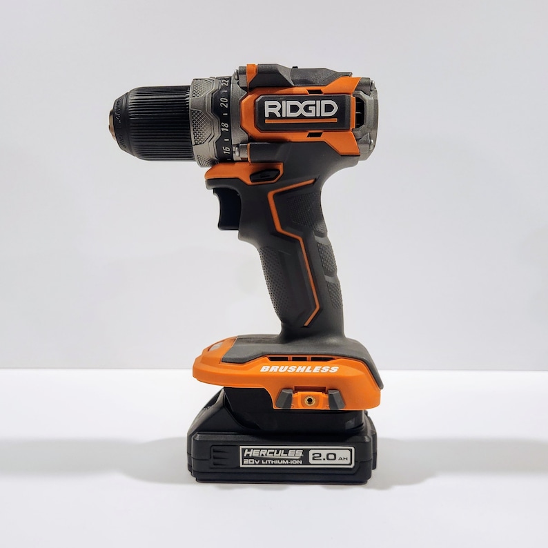 May include: An orange and black cordless drill with a brushless motor and a 20V lithium-ion battery. The drill has a black handle and a black and orange trigger. The battery is labeled "Hercules 2.0 Ah".