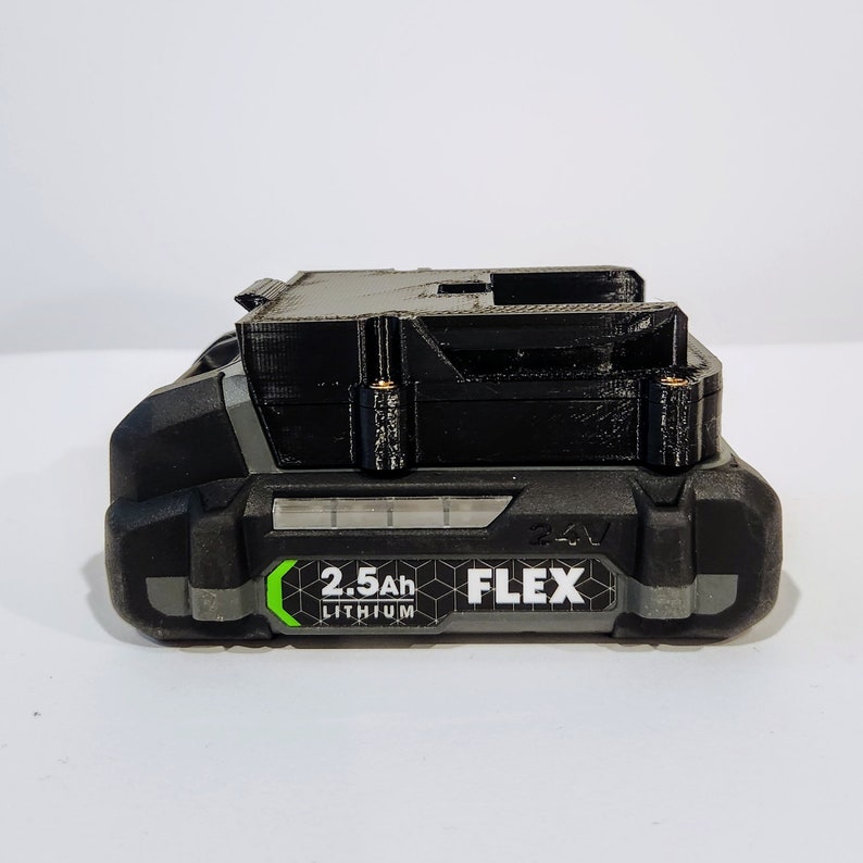 Puede incluir: Una bater&iacute;a de herramienta el&eacute;ctrica negra y gris con una etiqueta verde que dice "2.5Ah Lithium FLEX 24V".
