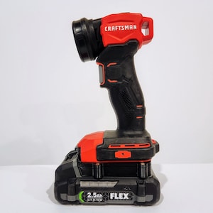 May include: A red and black cordless work light with a built-in battery pack. The light has a handle and a large, round head. The battery pack is labeled "2.5Ah Lithium FLEX" and is attached to the bottom of the light.
