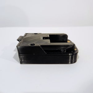 Op de afbeelding: Een zwarte 3D-geprinte batterijhouder met een vergrendeling aan de zijkant.