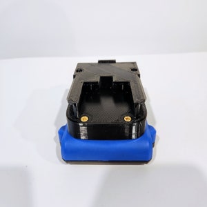 Op de afbeelding: Een zwarte 3D-geprinte batterijhouder met een blauwe rubberen basis. De houder heeft twee gouden schroeven aan de zijkant.