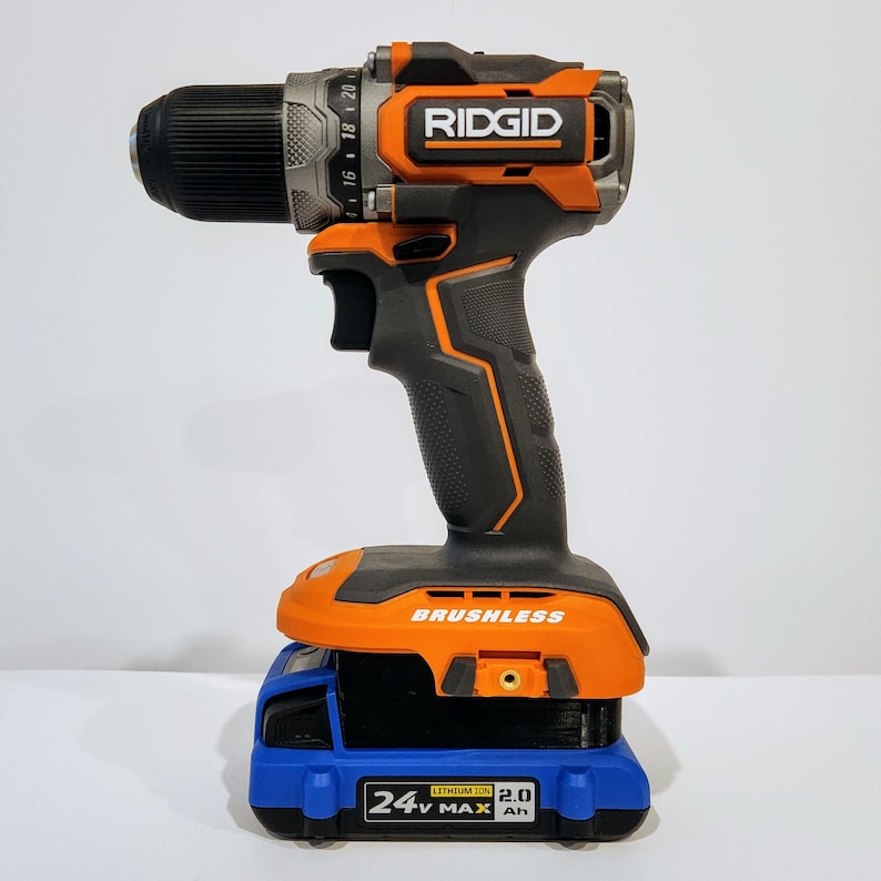 Op de afbeelding: Een zwarte en oranje draadloze boormachine met een borstelloze motor en een 24V MAX 2.0 Ah lithium-ion batterij. De boormachine staat op een blauwe batterijlader.