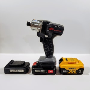 以下が含まれることがあります： 銀色のチャックが付いた黒と灰色のコードレスインパクトドライバー。ドライバーには「IR インガソールランド」のラベルが貼られています。3つのバッテリーが付属しています。黒色のバッテリーには「Hercules 2.0」のラベルが貼られ、灰色のバッテリーには「Bauer 20v HYPERMAX リチウムイオン 1.5Ah」のラベルが貼られ、黄色のバッテリーには「DeWalt 20v XR 4Ah」のラベルが貼られています。
