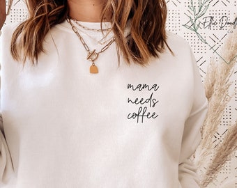 May include: White sweatshirt with the text "mama needs coffee" in black script.