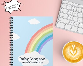 May include: A blue spiral bound notebook with a rainbow and clouds design. The text "Baby Johnson in the making" is printed on the cover.