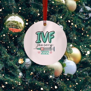 May include: A pink and white Christmas ornament with the text "IVF journey 2022" and a stylized image of a syringe with hearts on either side.