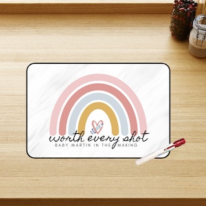 May include: A white background with a rainbow design in pink, blue, and yellow. The rainbow has a heart in the centre. The text "worth every shot" is below the rainbow, and the text "Baby Martin in the making" is below that.
