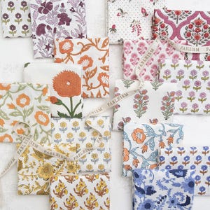 May include: A collection of folded fabric squares with various floral patterns in shades of orange, yellow, pink, purple, and blue. Some squares have a ribbon with the word "FABLEISM" printed on it.