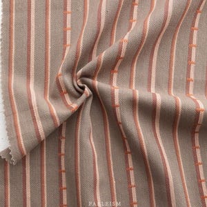 May include: Close-up of a striped fabric with brown, pink, and orange stripes. The fabric has a textured woven appearance.