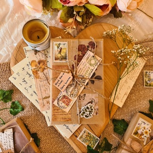 May include: A display of vintage stationery, including wrapped packages, stamps, and handwritten notes, arranged on a wooden heart-shaped board. The items are tied with twine and decorated with floral and botanical accents. A lit candle is also present.