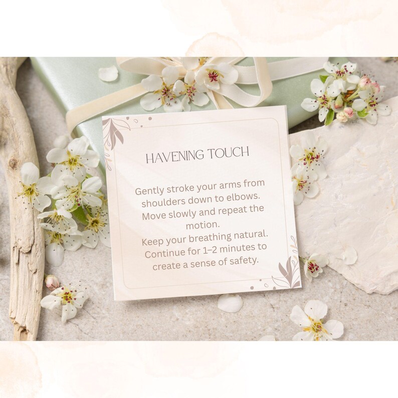 May include: A square card with the text "HAVENING TOUCH" and instructions for a self-soothing technique. The card is surrounded by white flowers and rests on a light-colored surface, with a wrapped gift in the background.