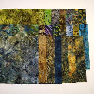 May include: A collection of rectangular fabric swatches featuring batik patterns in shades of green, blue, yellow, and brown. The assortment includes various textures and motifs, such as geometric shapes, organic swirls, and floral-like designs.