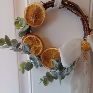 May include: A dried orange slice wreath with eucalyptus greenery and a white ribbon with a gold star charm.