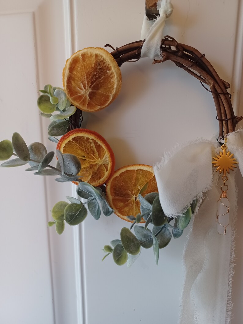 May include: A dried orange slice wreath with eucalyptus greenery and a white ribbon with a gold star charm.