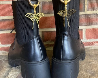 May include: A pair of black leather ankle boots with chunky heels and gold butterfly charms attached to the laces.