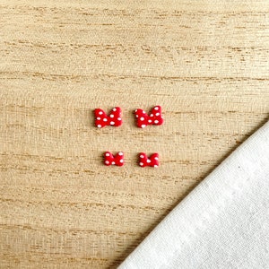 May include: Four red and white polka dot bow earrings on a wooden surface.