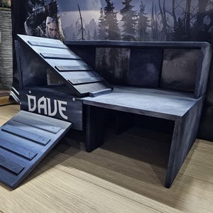 May include: A bespoke wooden pet habitat, painted in grey and blue tones, featuring a ramp and platform. The name "DAVE" is stenciled in white. The habitat is designed for small pets, with a ramp and platform.