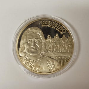 May include: A gold-colored coin featuring a portrait of Geronimo, with the text "GERONIMO BEDONKOHE APACHE" and the years "1829-1909". The coin is encased in a clear plastic holder.
