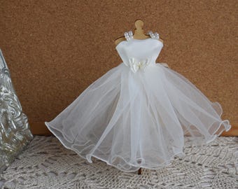 May include: A white tulle wedding dress with a satin bodice and a bow at the waist. The dress is on a wooden mannequin with pearl accents.