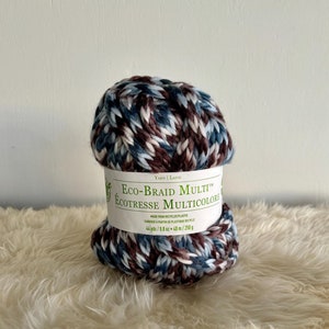 K&ouml;nnte beinhalten: Eine Garnrolle mit mehrfarbigen Garn in Blaut&ouml;nen, Braun und Wei&szlig;. Das Garn ist mit "Eco-Braid Multi&trade; EcoTresse Multicolore" gekennzeichnet und besteht aus recyceltem Kunststoff. Es enth&auml;lt 40 Meter / 250 Gramm.