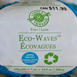 May include: A skein of Loops & Threads Eco-Waves yarn in a bright blue color. The label reads "Eco-Waves &Eacute;covagues" and "Limited Time Only P&eacute;riode Limit&eacute;e Seulement". The yarn is made from recycled plastic and contains 496 yards or 7 ounces (453 meters or 200 grams).