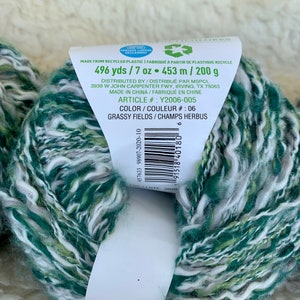May include: A skein of green, white, and light green yarn with a label that reads "496 yds / 7 oz &bull; 453 m / 200 g" and "GRASSY FIELDS / CHAMPS HERBUS".