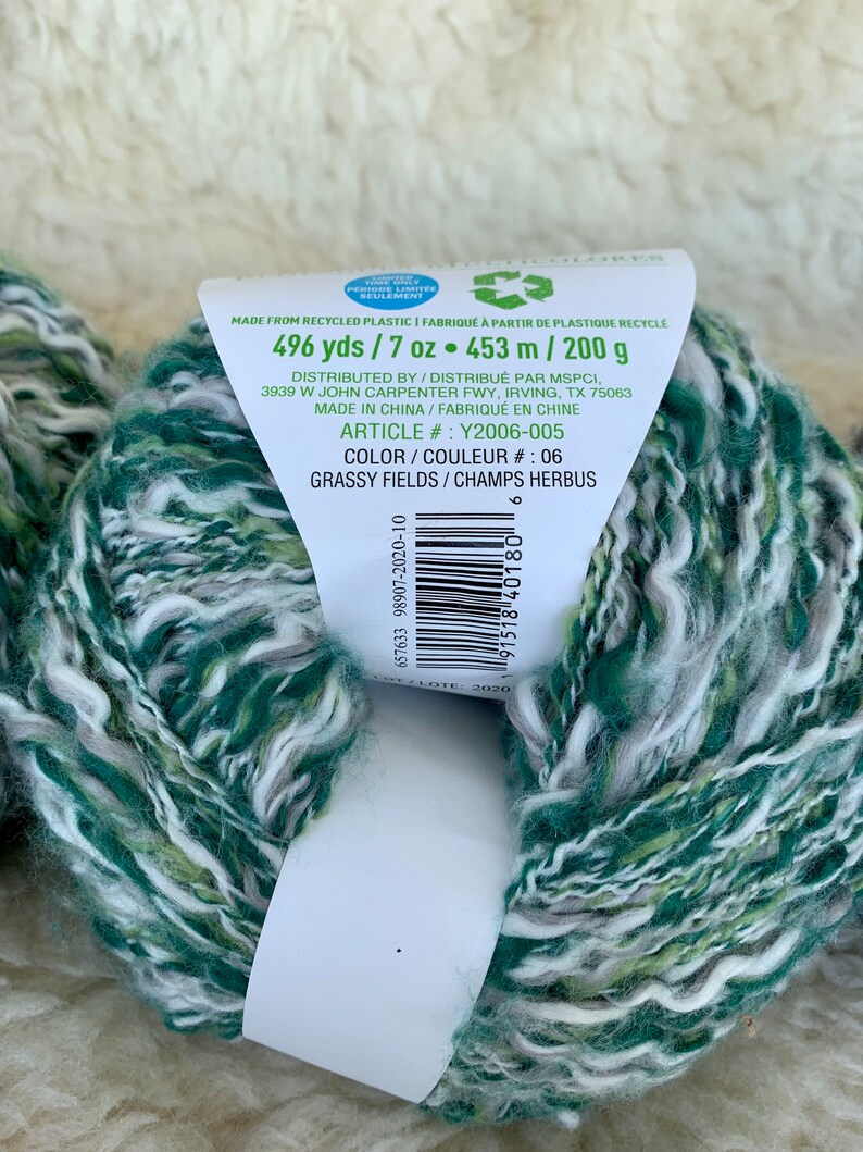 May include: A skein of green, white, and light green yarn with a label that reads "496 yds / 7 oz &bull; 453 m / 200 g" and "GRASSY FIELDS / CHAMPS HERBUS".