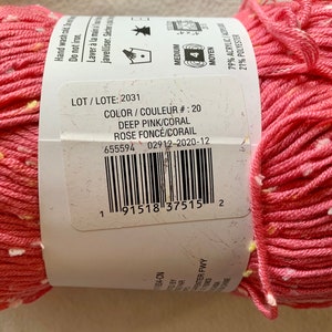 Peut inclure: Une pelote de fil rose fonc&eacute; avec des points blancs et jaunes. L'&eacute;tiquette indique "LOT/LOTE: 2031", "COLOR/COULEUR #: 20", "DEEP PINK/CORAL", "ROSE FONC&Eacute;/CORAIL", "655594 02912-2020-12", et "79% ACRYLIC/21% POLYESTER".