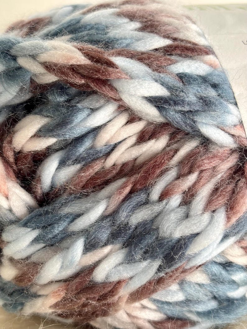 K&ouml;nnte beinhalten: Nahaufnahme eines Kn&auml;uels Garn in einer Farbkombination aus Blau, Wei&szlig; und Rosa. Das Garn ist weich und flauschig mit einer dicken Textur.