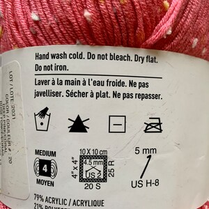 Peut inclure: Un pelote de laine rose avec des points blancs et jaunes. La laine est compos&eacute;e de 79% d'acrylique et de 21% de polyester. L'&eacute;tiquette indique un fil de poids moyen avec une taille d'aiguille recommand&eacute;e de US 2 (4,5 mm) et un &eacute;chantillon de 20 mailles et 25 rangs pour 10 cm (4 pouces). L'&eacute;tiquette comprend &eacute;galement des instructions d'entretien : lavage &agrave; la main &agrave; froid, ne pas blanchir, s&eacute;cher &agrave; plat et ne pas repasser.