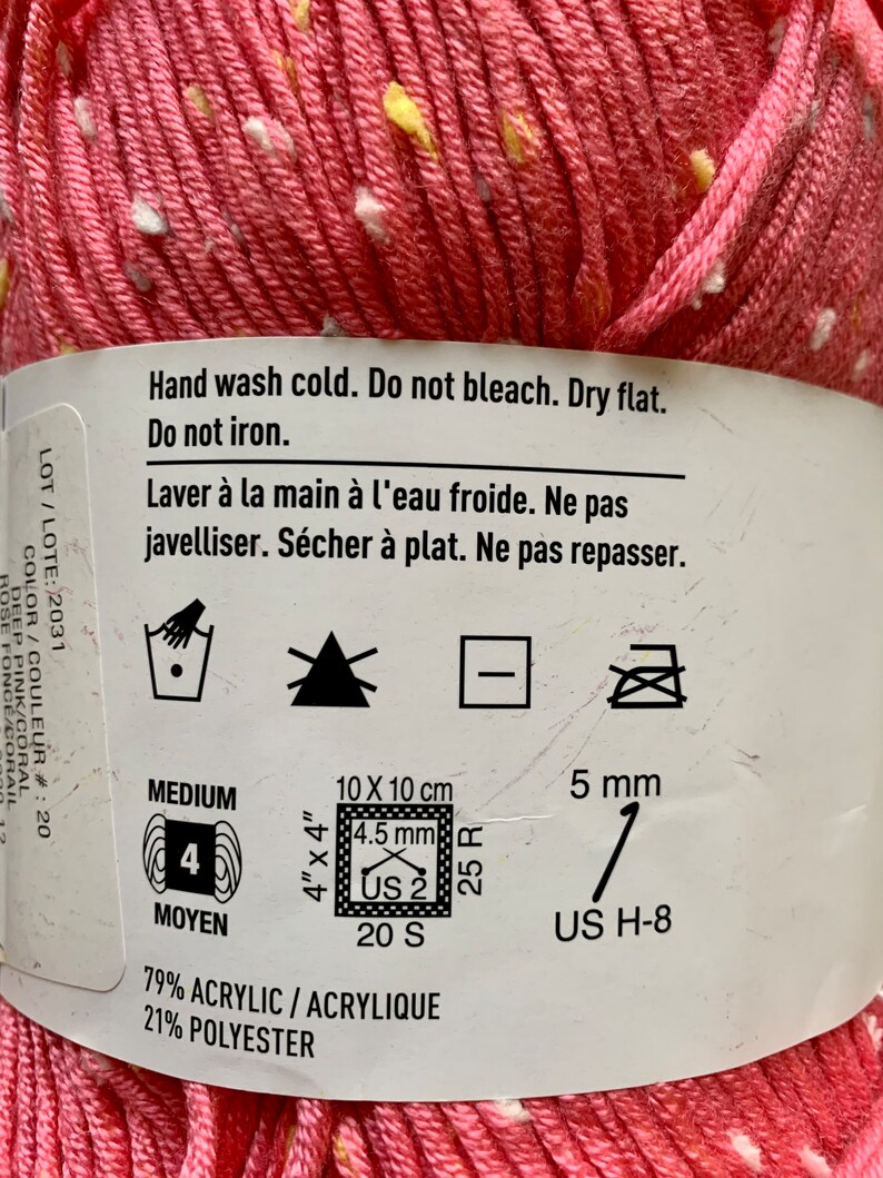 Peut inclure: Un pelote de laine rose avec des points blancs et jaunes. La laine est compos&eacute;e de 79% d'acrylique et de 21% de polyester. L'&eacute;tiquette indique un fil de poids moyen avec une taille d'aiguille recommand&eacute;e de US 2 (4,5 mm) et un &eacute;chantillon de 20 mailles et 25 rangs pour 10 cm (4 pouces). L'&eacute;tiquette comprend &eacute;galement des instructions d'entretien : lavage &agrave; la main &agrave; froid, ne pas blanchir, s&eacute;cher &agrave; plat et ne pas repasser.