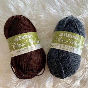 Può includere: Due gomitoli di lana Patons Classic Wool DK Superwash. Un gomitolo è marrone e l'altro è grigio.