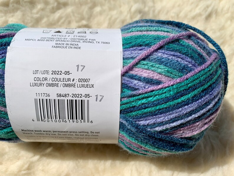 May include: A ball of yarn with a label that reads "LOT/LOTE: 2022-05-17 COLOR/COULEUR #: 02007 LUXURY OMBRE/OMBR&Eacute; LUXUEUX 111736 58487-2022-05-17" The yarn is a mix of blue, green, and purple shades.