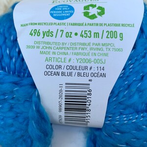 May include: A skein of blue yarn made from recycled plastic. The label reads "Eco-Waves Ecovagues" and includes the text "496 yds / 7 oz &bull; 453 m / 200 g" and "Color/Couleur #: 114 Ocean Blue/Bleu Oc&eacute;an".