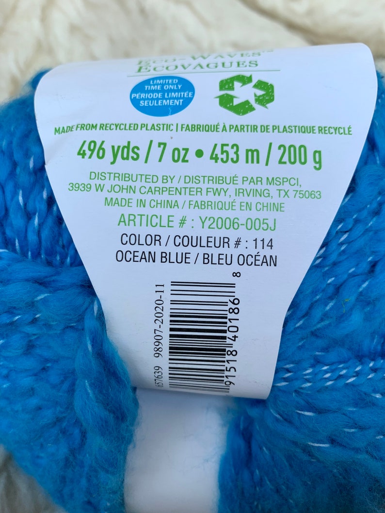 May include: A skein of blue yarn made from recycled plastic. The label reads "Eco-Waves Ecovagues" and includes the text "496 yds / 7 oz &bull; 453 m / 200 g" and "Color/Couleur #: 114 Ocean Blue/Bleu Oc&eacute;an".