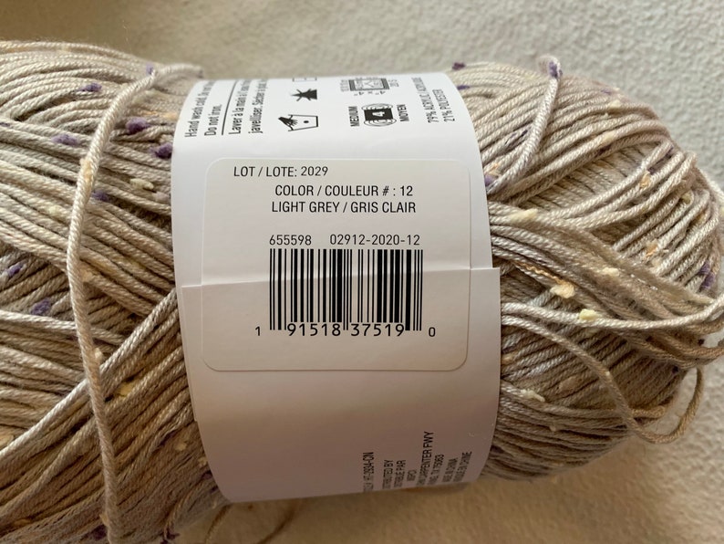Peut inclure: Une pelote de fil gris clair avec une &eacute;tiquette blanche qui indique "LOT/LOTE: 2029", "COLOR/COULEUR #: 12", "LIGHT GREY/GRIS CLAIR", "655598 02912-2020-12", et un code-barres.