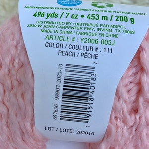 May include: A pink yarn ball with a label that reads "496 yds / 7 oz. 453 m / 200 g", "Distributed by / Distribu&eacute; par MSPCI, 3939 W John Carpenter Fwy, Irving, TX 75063", "Made in China / Fabriqu&eacute; en Chine", "Article #: Y2006-005J", "Color / Couleur #: 111", "Peach / P&ecirc;che", "657636 98907-2020-10", "91518 40183", "LOT / LOTE: 202010".