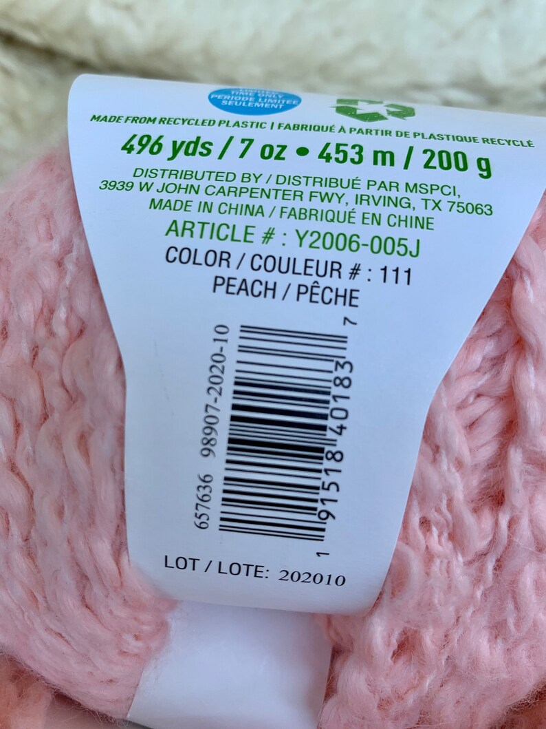May include: A pink yarn ball with a label that reads "496 yds / 7 oz. 453 m / 200 g", "Distributed by / Distribu&eacute; par MSPCI, 3939 W John Carpenter Fwy, Irving, TX 75063", "Made in China / Fabriqu&eacute; en Chine", "Article #: Y2006-005J", "Color / Couleur #: 111", "Peach / P&ecirc;che", "657636 98907-2020-10", "91518 40183", "LOT / LOTE: 202010".