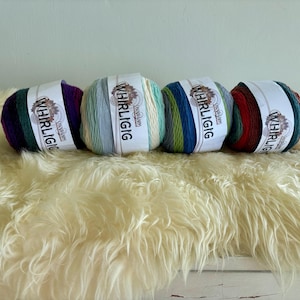 May include: Four skeins of multi-coloured yarn, each labelled "Whirligig". The yarn features shades of purple, green, blue, red, and white. They are displayed on a fluffy, cream-coloured surface.